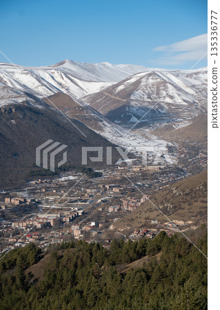 Panoramic view of Goris in Armenia, nestled between mountains with snow-covered peaks, layered hills, urban buildings, clear winter light Panoramic view of Goris in Armenia, nestled between mountains with snow-covered peaks, layered hills, urban buildings, clear winter light 135336777