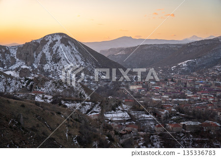Sunset view over Goris, Armenia, seen from hotel viewpoint, with snow-dusted hills, rocky slopes, red-roof houses, warm evening sky 135336783
