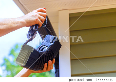 Contractor is attaching gutter piece to house in bright weather while working on home maintenance. Contractor is attaching gutter piece to house in bright weather while working on home maintenance. 135336850