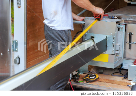 Gutter worker measures long metal rain gutter system with ruler while working inside 135336853
