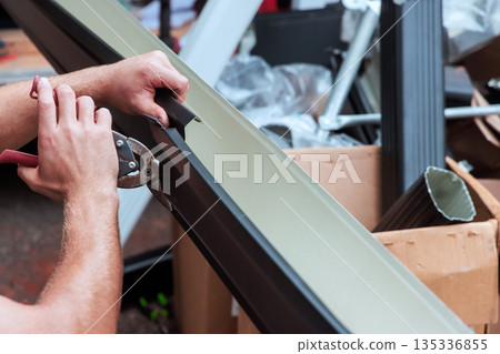 Metal worker uses tools to cut gutter channels metal trim in busy workshop with tools materials. Metal worker uses tools to cut gutter channels metal trim in busy workshop with tools materials. 135336855