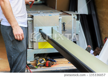 Worker uses machine to fabrication aluminum gutter channels in workshop tools equipment 135336857