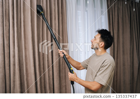 Man professionally steam cleaning curtains in modern home, providing deep drapery maintenance and effective dry cleaning for textile hygiene and fresh living space. 135337437
