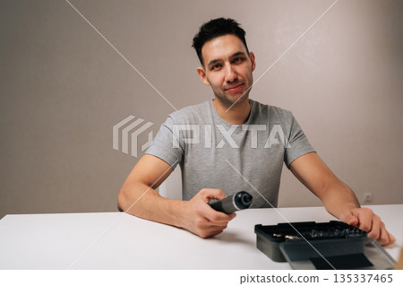 Happy young man demonstrating cordless screwdriver, smiling looking camera illustrating home improvement, diy projects, everyday repairs, positive customer experience with versatile mini power tool. 135337465