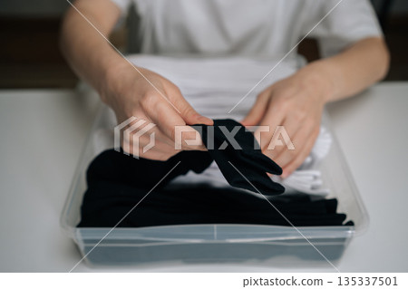 Person organizing laundry, neatly folding fresh black socks and arranging them into clear storage bin, prioritizing tidiness, home management, and efficient closet order, close-up cropped shot. 135337501