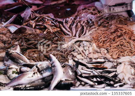 Fresh Seafood Display At Market Stall: Raw Fish, Squid, And Shellfish Arranged In White Crates On Ice In Indoor Food Market Setting 135337605