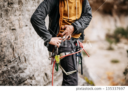Rock Climber Attaching Ohm Device To Harness: Taped Fingers, Safety Equipment, And Rope System During Preparation At Natural Rock Wall 135337697