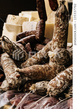 Traditional Cured Sausages At Market Stall: Rustic Dry Meat Products Displayed In Abundant Arrangement With Natural Texture And Warm Light 135337702