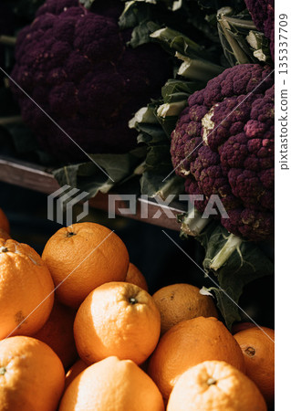 Strong Color Contrast At Market Stall: Bright Orange Citrus Fruits In Foreground Against Dark Purple Cauliflower And Green Vegetables 135337709
