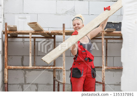 Woman carrying plank boards on construction site 135337891