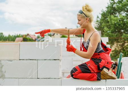 Woman using string as level in wall construction. Woman using string as level in wall construction. 135337905