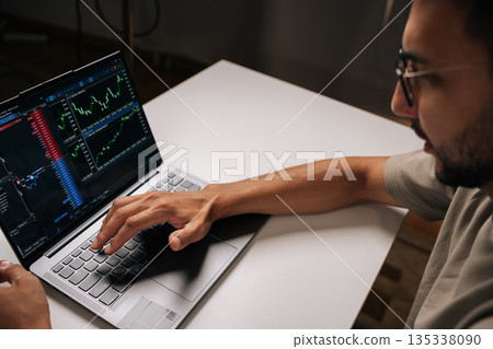 Close-up of trader in glasses typing on laptop keyboard, engaging in online trading and financial analysis, viewing real-time charts and data for informed investment decisions at home office. 135338090