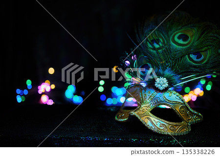 Masquerade mask with peacock feathers, bokeh lights, and mystery Masquerade mask with peacock feathers, bokeh lights, and mystery 135338226
