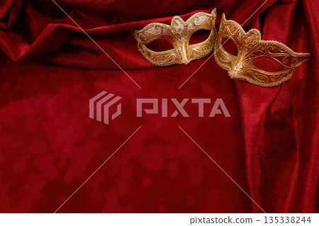 Golden masquerade masks resting on red velvet drapery 135338244
