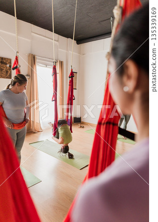 Women practicing aerial vinyasa yoga in studio 135339169