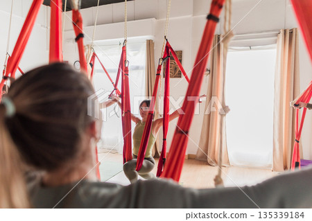 Woman practicing aerial yoga enjoying fitness class Woman practicing aerial yoga enjoying fitness class 135339184
