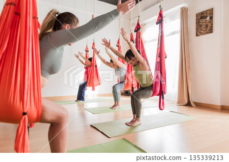 Multicultural women practicing aerial vinyasa yoga in hammocks 135339213
