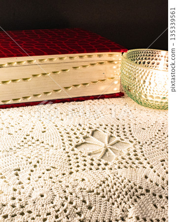 Red book with gilt page edges on a crocheted white tablecloth. Contemplative scene Red book with gilt page edges on a crocheted white tablecloth. Contemplative scene 135339561