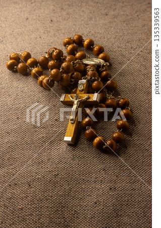 Wooden rosary with a metal crucifix featuring Jesus Christ's figure is resting on textured fabric 135339563