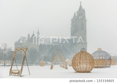 Winter scene Domplatz Magdeburg Dom cathedral silhouette snow fog background festive Lichterwelt light installation. Snow cover square cold weather holiday decoration historic architecture cityscape Winter scene Domplatz Magdeburg Dom cathedral silhouette snow fog background festive Lichterwelt light installation. Snow cover square cold weather holiday decoration historic architecture cityscape 135339805