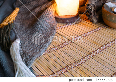 Warm salt lamp glow beside tasselled knitted textile and a bowl of stones in the background Warm salt lamp glow beside tasselled knitted textile and a bowl of stones in the background 135339880