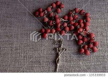 Rosary with red wooden beads and crucifix laying on a grey textured surface 135339933