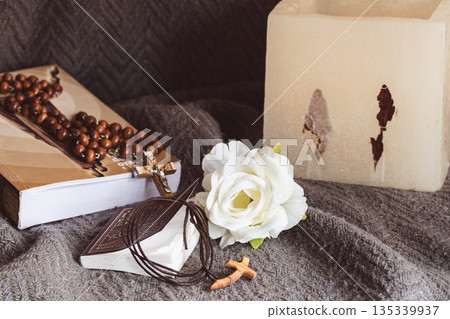 Christian still life, rosary on a Bible, small prayer book with wooden cross on textured gray fabric Christian still life, rosary on a Bible, small prayer book with wooden cross on textured gray fabric 135339937