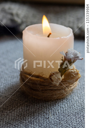 Candle glowing with a bright flame wrapped with natural jute on grey background 135339984