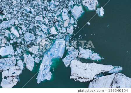 Floating icebergs of varying sizes and shapes scatter across turquoise waters, showcasing intricate cracks and textures in a glacial lagoon in Iceland. 135340104