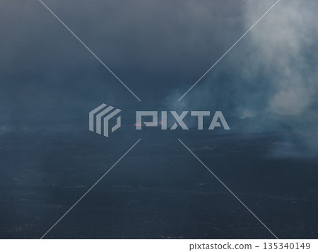 Dark landscape showing glowing lava and dense smoke from an active volcanic eruption in Iceland, with rugged terrain and geothermal activity. 135340149
