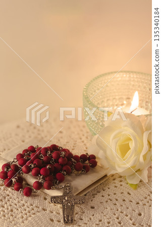 Christian faith objects showing spirituality and devotion, with a red rosary and lit candle 135340184