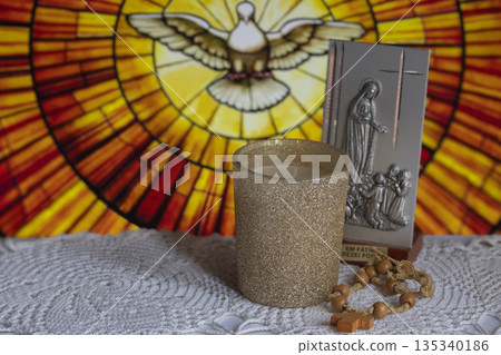 Religius items in the foreground with blurred stained glass dove of the Holy Spirit evoking faith, devotion and hope Religius items in the foreground with blurred stained glass dove of the Holy Spirit evoking faith, devotion and hope 135340186