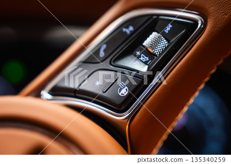 Tight close up of right side controls on a Bentley Bentayga Speed. Textured metal scroll wheel, voice, volume, and heated controls sit in tan leather with chrome trim. 135340259