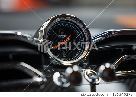 Close view of a Bentley Bentayga Speed dashboard clock shows winged B logo and BENTLEY EST. 1919 on a carbon fiber dial with orange hands, chrome trim, and soft lighting. Close view of a Bentley Bentayga Speed dashboard clock shows winged B logo and BENTLEY EST. 1919 on a carbon fiber dial with orange hands, chrome trim, and soft lighting. 135340275