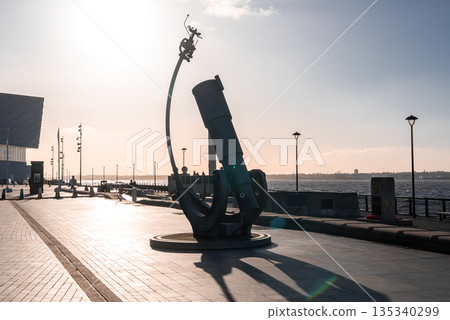 Liverpool waterfront at sunset shows the Liverpool Telescope sculpture, cyclist on arc, Mersey, lampposts, Museum of Liverpool, Pier Head, and winter light. 135340299