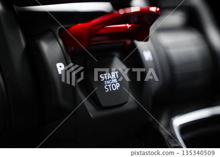 Close up shows Lamborghini Urus SE ignition switch with red flip up cover, START ENGINE STOP button, P gear marking, glossy black console, shallow depth of field. 135340509