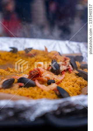 A steaming pan of seafood paella with mussels and shrimp is cooked and served at a Christmas market in Riga, Latvia, with soft winter light and drifting steam. 135340557