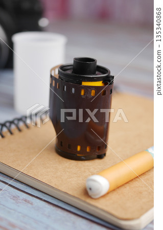 Film roll sits on notebook next to a camera and pen Film roll sits on notebook next to a camera and pen 135340868
