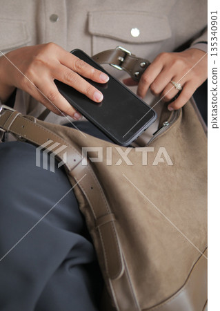 Hand putting smartphone into tan bag in indoor space 135340901