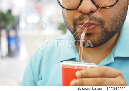Man drinking from a red cup with a straw in a cafe Man drinking from a red cup with a straw in a cafe 135340921