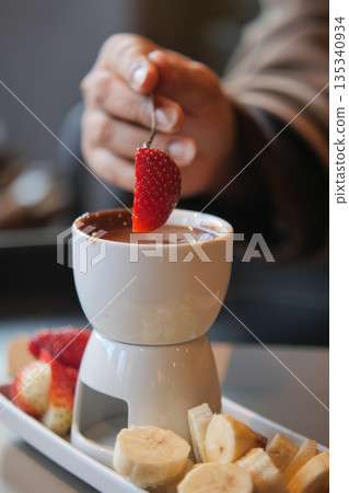 Dipping fruit in chocolate at a dessert cafe in the evening Dipping fruit in chocolate at a dessert cafe in the evening 135340934