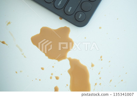 Coffee spill near keyboard on a white table surface Coffee spill near keyboard on a white table surface 135341007