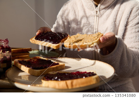 Person Spreading Peanut Butter and Jelly on Toasts for Breakfast Joy Person Spreading Peanut Butter and Jelly on Toasts for Breakfast Joy 135341080