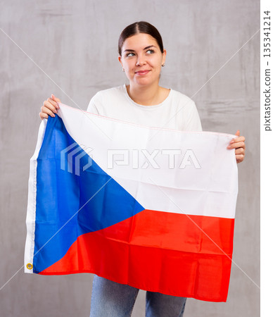 Joyous young woman holding Czech flag against unicoloured background Joyous young woman holding Czech flag against unicoloured background 135341214