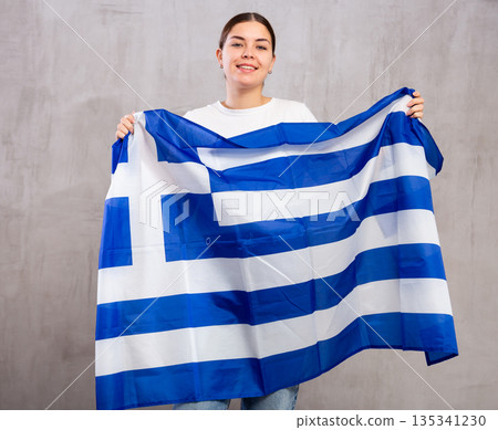 Joyous young woman holding Greece flag against unicoloured background Joyous young woman holding Greece flag against unicoloured background 135341230