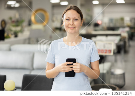 Woman wanders through furniture store with her mobile phone in hand Woman wanders through furniture store with her mobile phone in hand 135341234