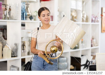 Smiling female purchaser choosing stylish table lamp in shop Smiling female purchaser choosing stylish table lamp in shop 135341237