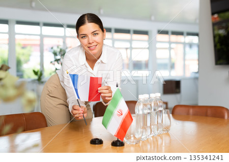 Positive young woman putting little flag of France on table next to the flag of Iran 135341241