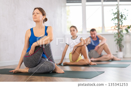 Happy middle-aged woman practicing lord of the fishes pose of yoga with her family Happy middle-aged woman practicing lord of the fishes pose of yoga with her family 135341253