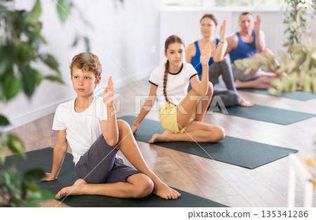 Middle-aged woman, man, preteen girl and boy practicing Marichi Pose, or Marichyasana on mats during family Hatha yoga class in wellness studio Middle-aged woman, man, preteen girl and boy practicing Marichi Pose, or Marichyasana on mats during family Hatha yoga class in wellness studio 135341286